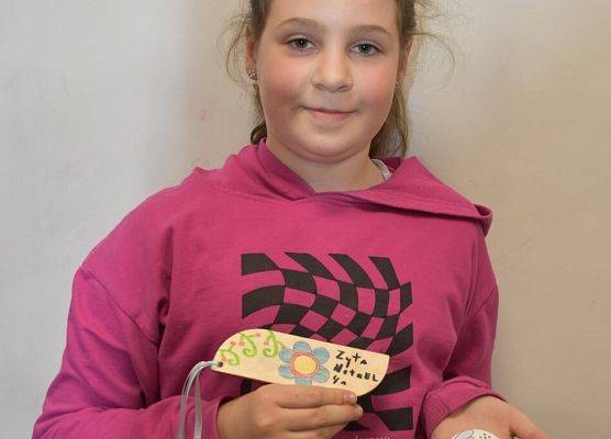 Dziewczynka prezentuje zakładkę i magnesik z motywami haftu kaszubskiego