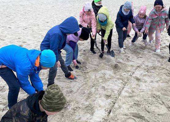 Grupa dzieci usypuje na plaży wał z piasku. (Fot. SP w J. Górze)