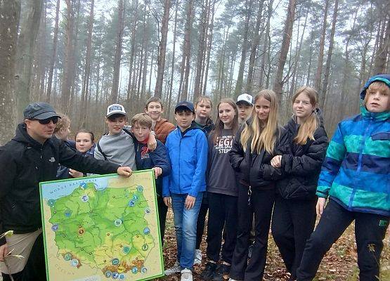 Zwarta grupa młodzieży oraz edukator trzymający dużą mapę Polski z zaznaczonymi Parkami Narodowymi