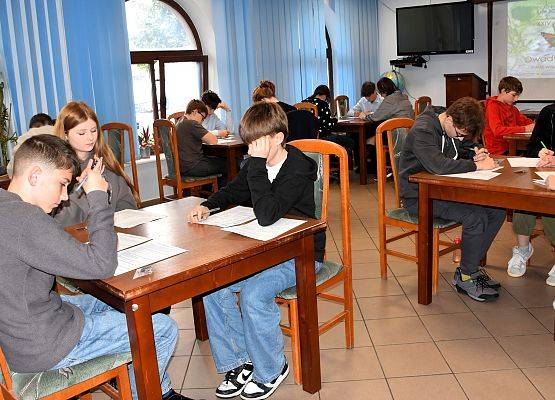 Siedzący przy stołach uczestnicy konkursy rozwiązującty test.