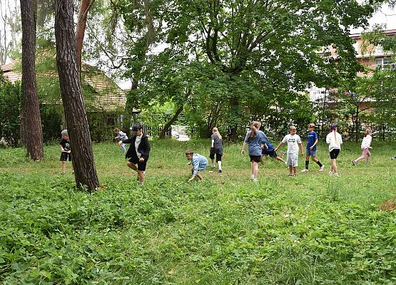 zajęcia w terenie zieleni - rozbiegane dzieci szukaja w trawie obrazków z tropami