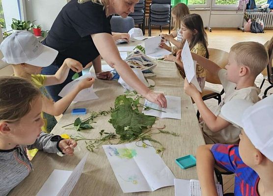 Grupa przy stolikach, na nich różne rośłiny i przybory plastyczne