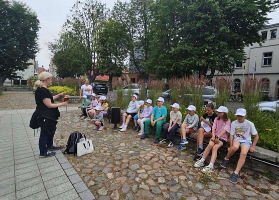 około 10 uczniów siedzi na ławce, na przeciwko pani botanik wyjaśnia na czym polega zadanie