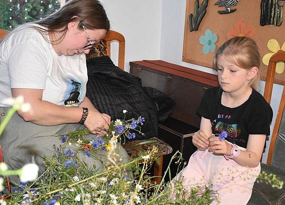 Pani z dziewczynką uplata wianek z kwiatów polnych m.in rumianki, chabry wrotycz